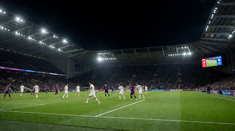 夜晚体育场内足球比赛进行中，看台灯光照亮绿茵球场